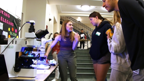 a woman standing next to a microscope presenting to Brain Bee participants
