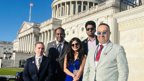 Four people in business attire standing outside the Capitol Building.