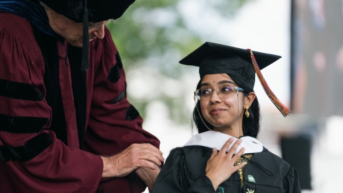 a man in regalia hooding a newly graduated masters student.