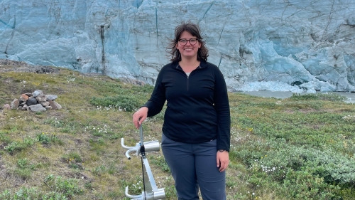 Woman standing in an open area with scientific instrument in hand.