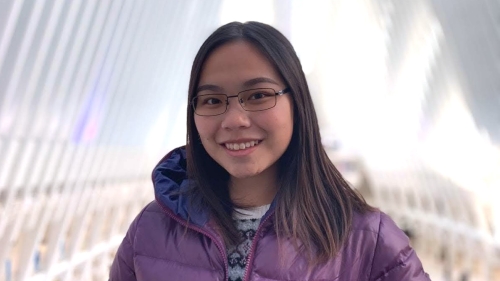 a woman with glasses in a purple coat standing outside.
