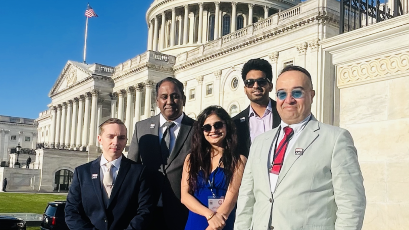 Four people in business attire standing outside the Capitol Building.