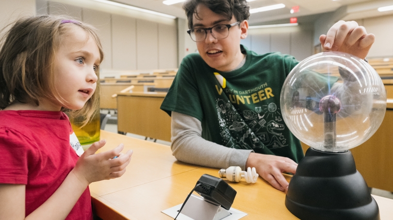 an adult with glasses demonstrating magnetic fields to a child in a red shirt.