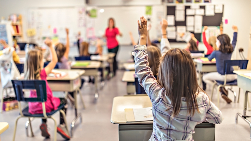 Young students in a classroom raising their hands