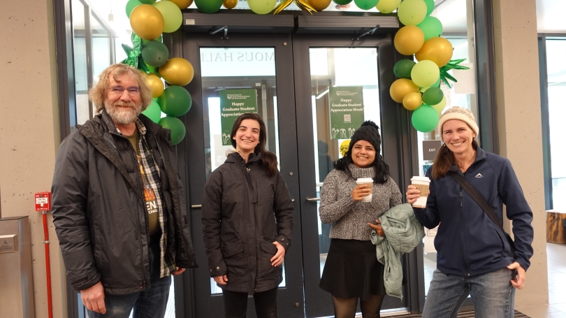 A man and three women stand under a green balloon arch smiling