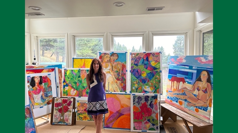 Nan Darham standing in front of a series of her colorful paintings.