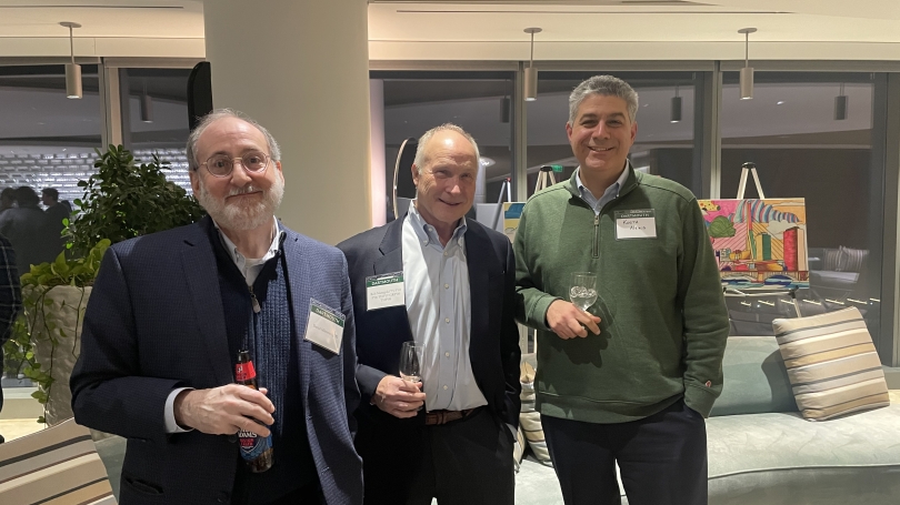 Three men standing in an event space smiling