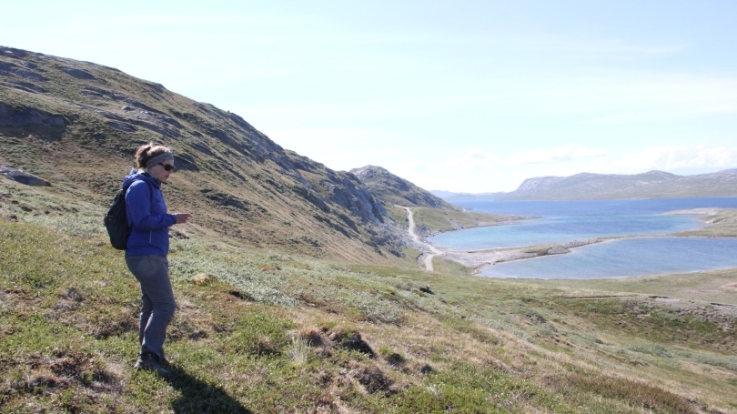 a student wearing a backpack who is standing on a scenic hillside near the shore.