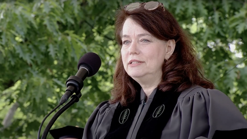 A woman in front of a microphone wearing graduation regalia