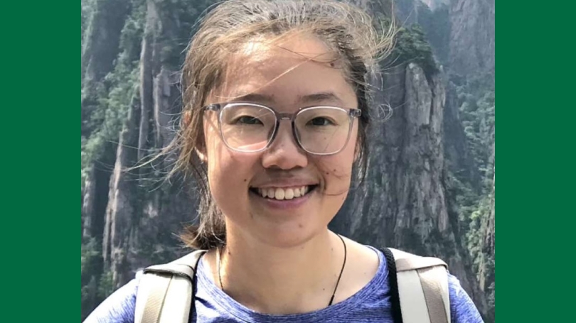 A smiling woman with glasses standing outside in front of mountains