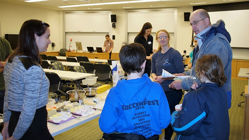 two graduate students showing a parent and his children the science behind bread and cheese